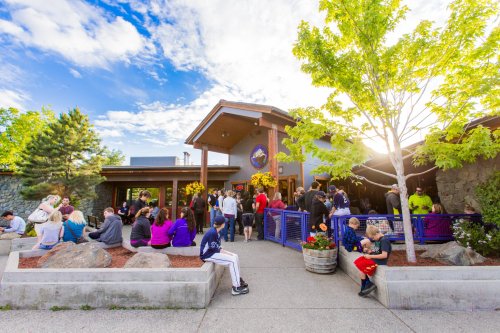 A busy restaurant entrance with people gathered outside, colorful flowers, and a clear blue sky.