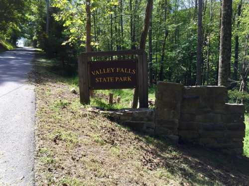 Sign for Valley Falls State Park beside a tree-lined road, with greenery surrounding the area.