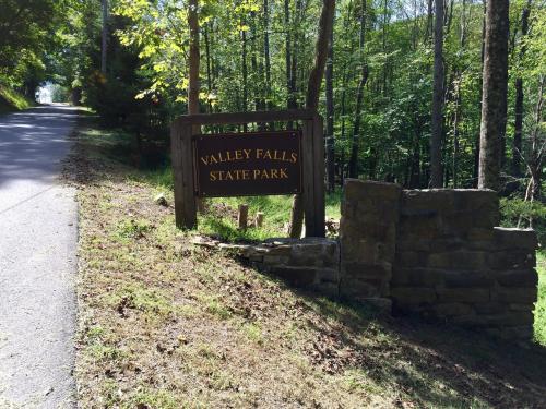 Sign for Valley Falls State Park beside a tree-lined road, with greenery surrounding the area.
