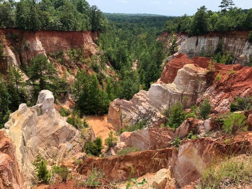 A scenic view of a colorful canyon with steep, layered cliffs and lush greenery in the background.