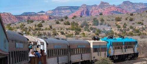 A vintage train travels through a desert landscape with colorful rock formations in the background.