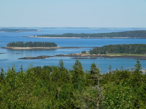 A scenic view of islands surrounded by blue water, with lush green trees in the foreground and a clear sky above.