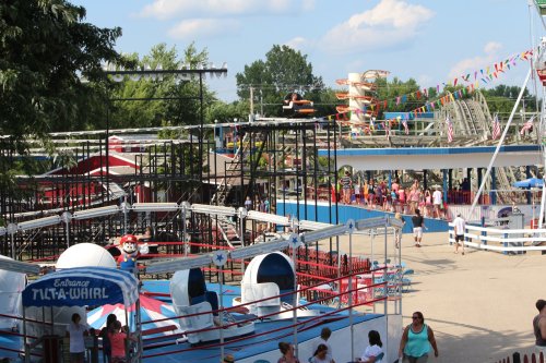 A vibrant amusement park scene featuring rides, colorful decorations, and visitors enjoying a sunny day.