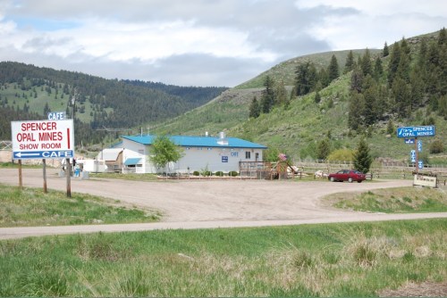 A small building with a blue roof, surrounded by greenery, featuring signs for a café and opal mine showroom.
