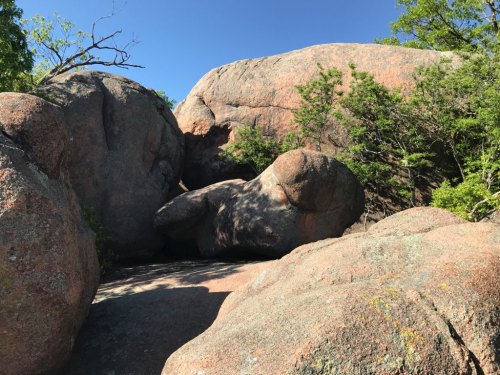 Large boulders surrounded by trees under a clear blue sky, showcasing natural rock formations.
