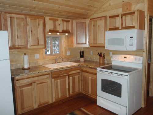 Cozy wooden kitchen with natural wood cabinets, granite countertops, a sink, microwave, and stove.