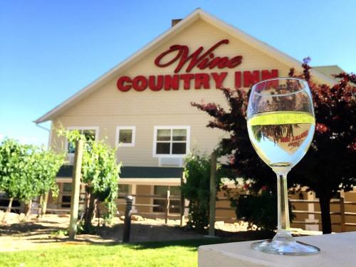 A glass of white wine in front of the Wine Country Inn, surrounded by vineyards and a clear blue sky.