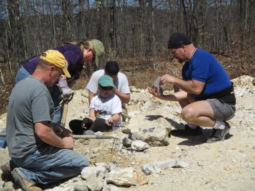 A group of five people excavating in a rocky area, focused on digging and examining fossils or artifacts.