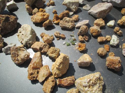 A variety of colorful rocks and minerals scattered on a dark surface, showcasing different shapes and textures.