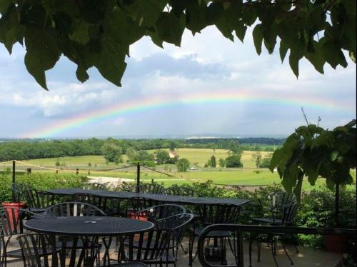 A scenic view of a rainbow arching over green fields, seen from a patio with black metal tables and chairs.