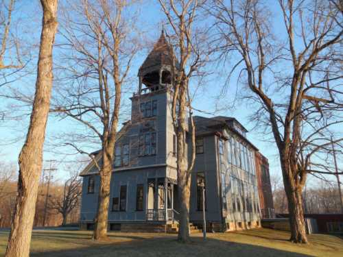 A tall, historic blue house with a tower, surrounded by bare trees against a clear sky.