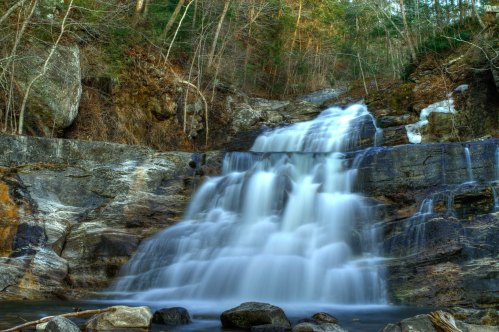 A serene waterfall cascading over rocky cliffs, surrounded by lush greenery and trees.