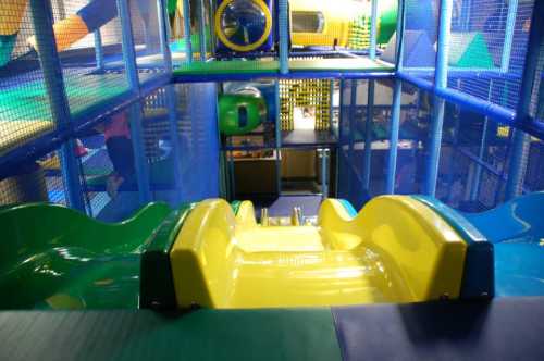 Colorful indoor play structure featuring green and yellow slides and a mesh enclosure.