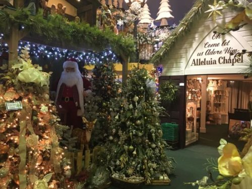 A festive display featuring Christmas trees, decorations, and a Santa figure near a chapel entrance.