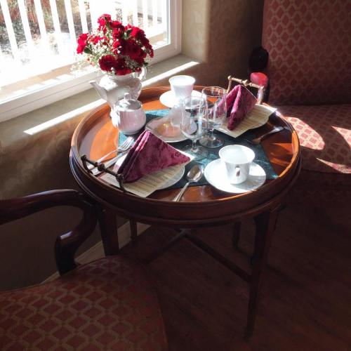 A cozy table setting by a window with flowers, glassware, and neatly folded napkins.