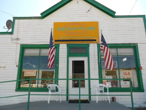 A small white building with green trim, featuring an "Open" sign and two American flags at the entrance.