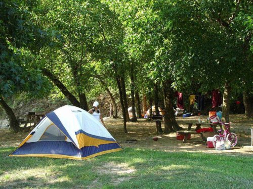 A campsite with a tent, picnic table, and children playing near trees, with clothes hanging to dry in the background.