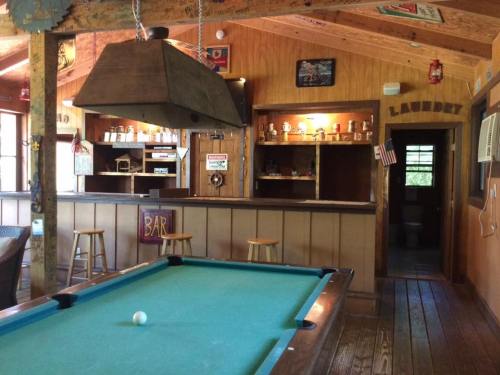 A rustic bar area with a pool table, wooden beams, and shelves displaying drinks in a cozy, inviting space.