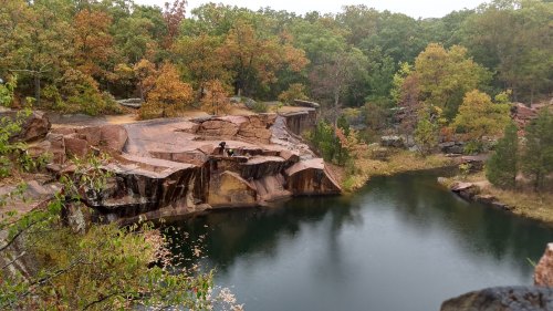 A serene quarry with a calm pond surrounded by autumn-colored trees and rocky cliffs.