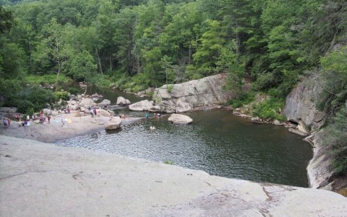 A scenic view of a river surrounded by rocks and lush greenery, with people enjoying the water.