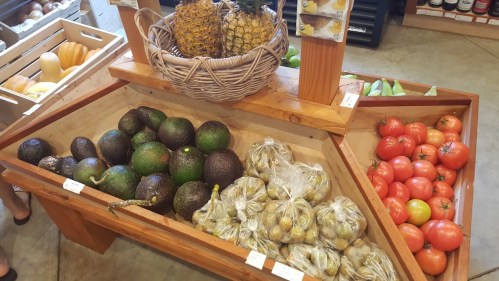 A wooden display featuring avocados, tomatoes, and a basket of pineapples in a market setting.