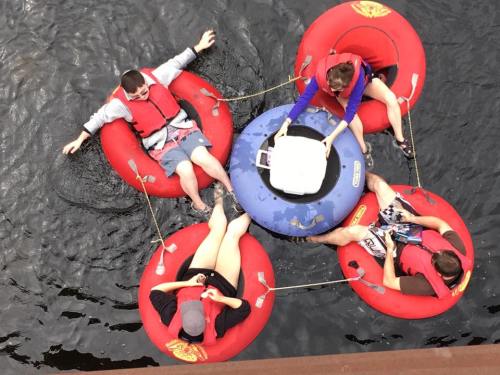 Four people in red inner tubes floating on water, gathered around a blue cooler in the center.