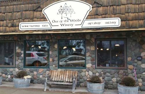 Exterior of Out of the Woods Winery, featuring a stone facade, wooden sign, and a rustic bench in front.