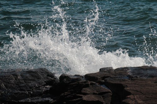 Waves crashing against dark rocks, creating splashes in a blue ocean.