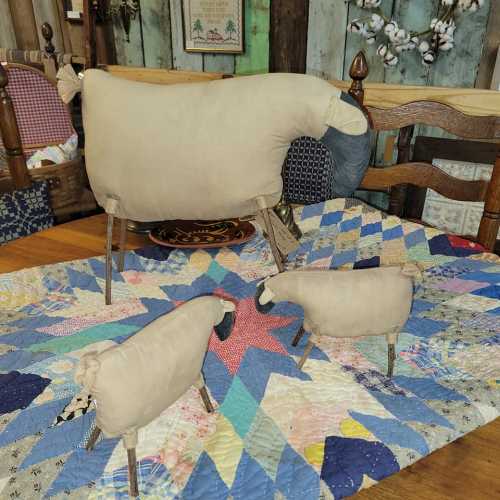 Three decorative sheep figures made of fabric and wood, placed on a colorful quilted tablecloth.