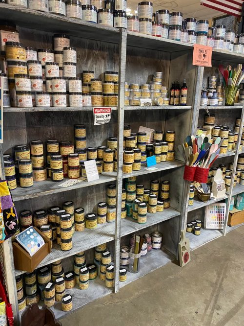 A wooden shelf filled with various jars and containers, alongside colorful kitchen utensils and a warning sign.