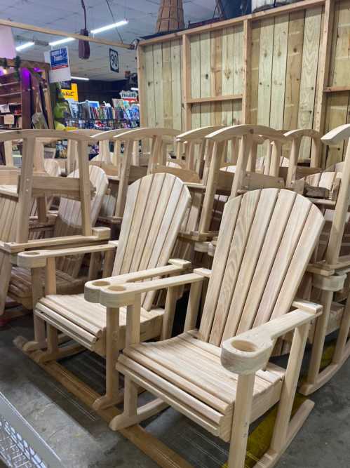 A row of unfinished wooden Adirondack chairs stacked in a store, showcasing their classic design and natural wood color.