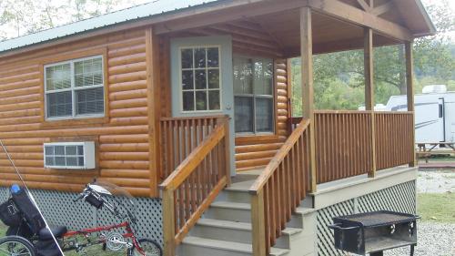 A wooden cabin with a porch, steps, and an air conditioning unit, surrounded by outdoor space and a bicycle.