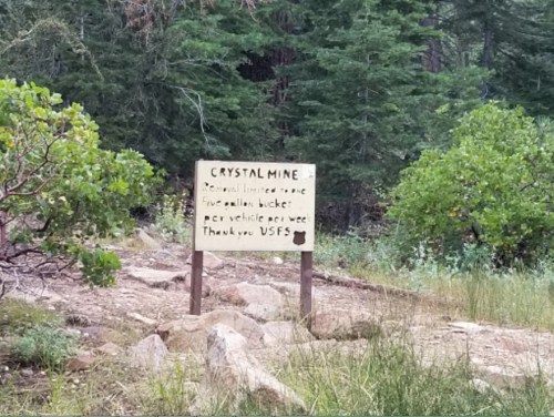 Sign for Crystal Mine with text about vehicle access, surrounded by greenery and rocky terrain.
