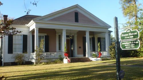 Historic pink house with white columns, surrounded by greenery, featuring a sign for the Stone House and music room.