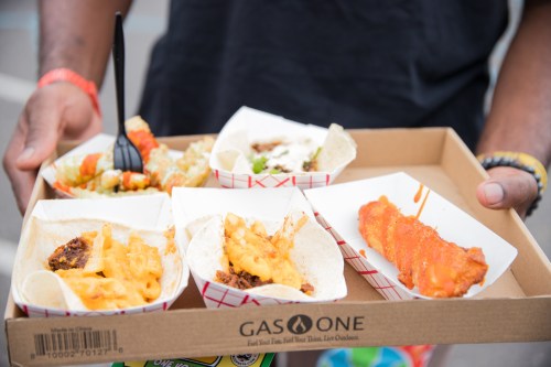 A person holds a tray with five taco-style dishes, featuring various toppings and sauces.