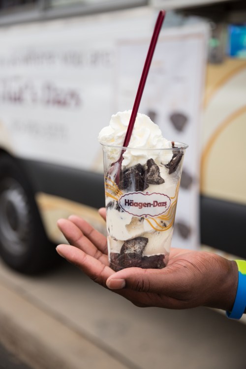 A hand holding a cup of Häagen-Dazs ice cream topped with whipped cream and chocolate pieces.