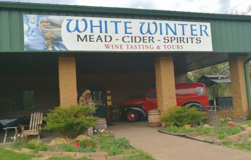 Sign for White Winter Mead, Cider, and Spirits with a red vintage truck and outdoor seating area.