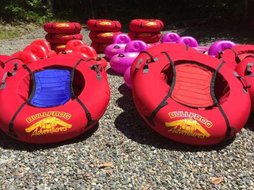 A collection of red and pink inflatable tubes arranged on a gravel surface, ready for water activities.