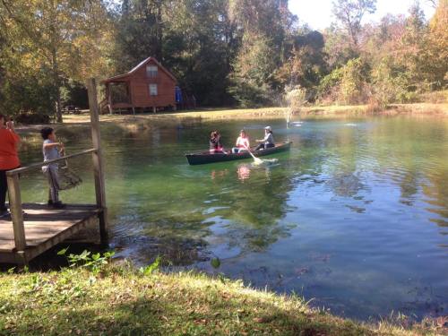 A group of people canoeing on a calm pond, with a wooden cabin and trees in the background.