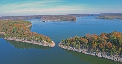 Aerial view of a serene lake surrounded by colorful autumn foliage and rocky shorelines under a clear blue sky.