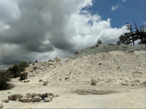 A rocky landscape with a hill, scattered boulders, and a cloudy sky in the background.