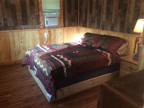 Cozy bedroom with a wooden accent wall, a bed with a patterned quilt, and a bedside lamp.