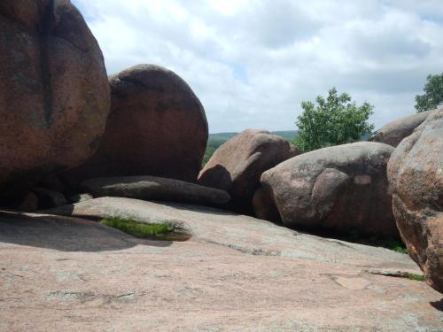 Large, smooth boulders scattered across a rocky landscape under a cloudy sky, with greenery in the background.