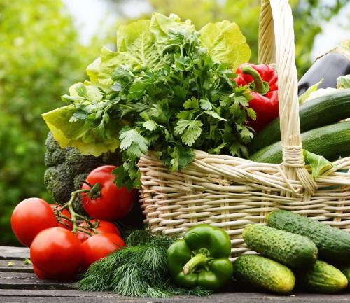 A woven basket filled with fresh vegetables, including tomatoes, cucumbers, bell peppers, and leafy greens.