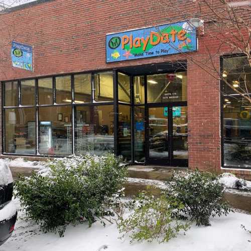 Exterior of PlayDate building with colorful signage, surrounded by snow and greenery.