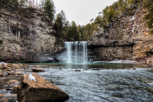 A serene waterfall cascades into a tranquil pool, surrounded by rocky cliffs and lush greenery.
