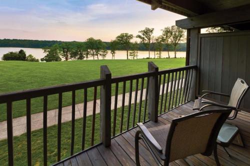 A serene balcony view overlooking a grassy area and a calm lake, framed by trees under a soft sunset sky.