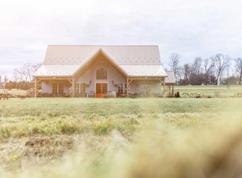 A modern farmhouse with a bright orange door, surrounded by a grassy field and trees in the background.