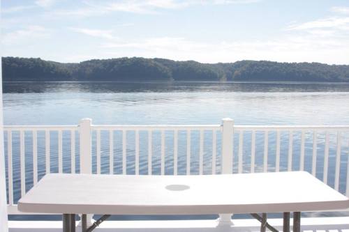 A table on a deck overlooking a calm lake with hills in the background under a clear blue sky.