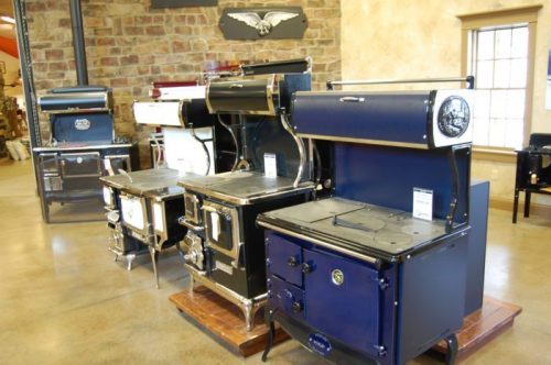 A display of vintage-style kitchen stoves in various colors and designs, set in a rustic interior.